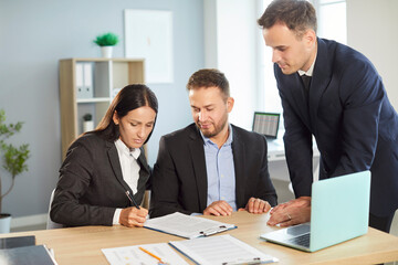 Coworkers gather in an office, signing a contract during a meeting. Formal deal, fostering agreement, partnership, and teamwork through active collaboration in a professional setting.