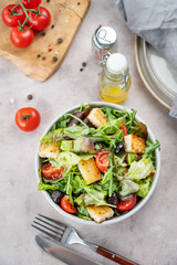 Vegetable salad with lettuce, tomatoes, croutons and olives in a bowl on a light background