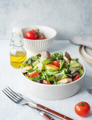 Vegetarian salad with lettuce, tomatoes, croutons and olives in a bowl on a light background