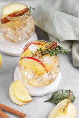 Apple cocktail or cider with cinnamon stick and thyme garnish on light background