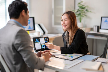 A man and a woman are sitting at a desk with a laptop and a tablet