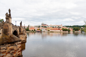 A picturesque view of Prague Castle and surrounding historical architecture, with reflections on the Vltava River under a cloudy sky