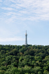 A wide-angle view of Prague’s iconic red rooftops, historic churches, and lush green surroundings. The cityscape combines traditional architecture with glimpses of modern structures in the background
