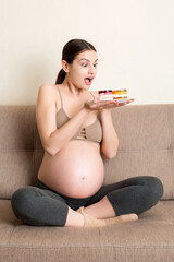 Excited pregnant woman is eating cakes with great pleasure relaxing at home. Enjoying sweet food during pregnancy concept