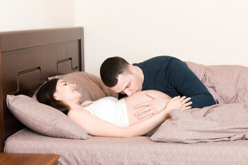 Loving pregnant couple kiss on bed in morning