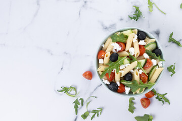 Mediterranean Pasta Salad in bowl on white marble background. Top view. Copy space