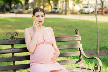 pregnant woman sits on a park bench and talking on phone