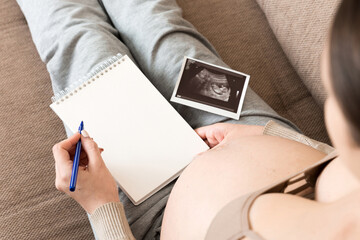 Top view caring future mother writing diary with ultrasound. pregnant woman tummy making notes feeling during pregnancy or creating scrapbook