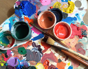 An artist's messy yet vibrant palette holds a variety of colorful paints, brushes, and mixing pots, capturing the creative energy of the painting process.