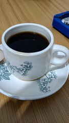 Photo of black coffee in a white and patterned cup. Black coffee. Black coffee as a casual companion. Black coffee in a white ceramic cup with a pattern. Raw photo.