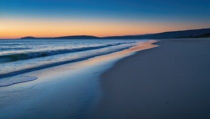 A tranquil beach at sunset, where golden hues merge into a wide blue sky. Soft waves ripple onto the shore, and footprints in the sand trail toward the horizon, evoking a peaceful, everlasting beauty.