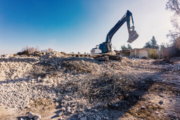 Excavator with bucket separating concrete debris from metal rebar and compressing it for recycling...