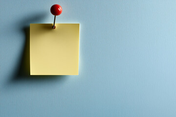 Yellow Sticky Note Pinned on Light Blue Wall with Red Pushpin, Office Reminder