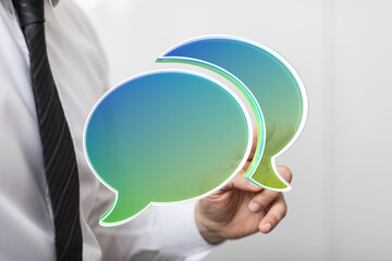 Image depicts a businessman's hand holding two transparent speech bubbles, symbolizing...