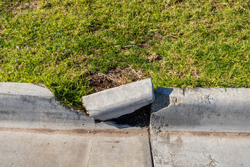 A broken concrete kerb with a dislodged section next to a grass verge along a suburban footpath or...