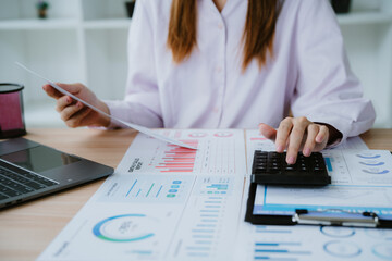Fototapeta premium Businesswoman analyzing financial charts and using calculator in office