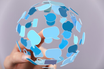 Abstract image of a hand interacting with a sphere of blue speech bubbles, representing global...