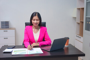 Cheerful business lady working on laptop in office, Asian happy beautiful businesswoman in formal suit work in workplace. Attractive female employee office worker smile.