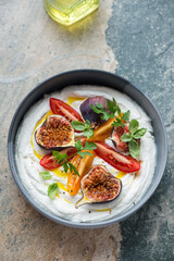 Bowl of ricotta dipping sauce with fresh fig fruits and tomatoes, vertical shot on a beige and grey granite background, high angle view