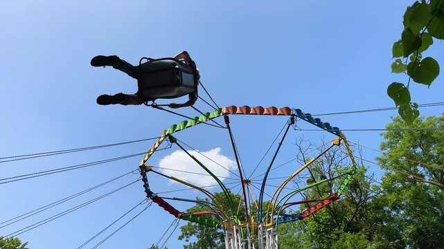 Low-angle view of a kids flying high on a colorful chain swing carousel ride against a blue sky.Carefree summer fun: A riders on a wave swinger attraction soars through the air at an amusement park