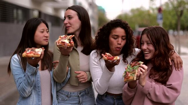 Three young women, likely friends or colleagues, enjoy slices of pizza while strolling down a city street, engaging in lively conversation and laughter