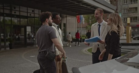 A multiracial business team discusses plans outside a hotel. They shake hands and walk towards the hotel entrance. - Powered by Adobe
