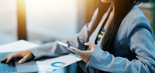 Fototapeta premium Asian businesswoman in formal suit in office happy and cheerful during using smartphone and working