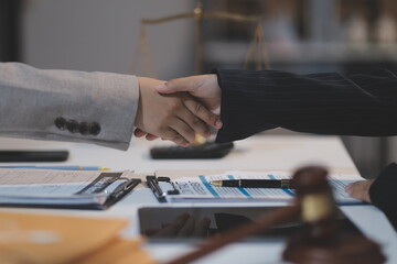 Lawyer shaking hands with a client making about documents, contracts, agreements, cooperation agreements with a female client at the lawyer's desk and a hammer at the table.