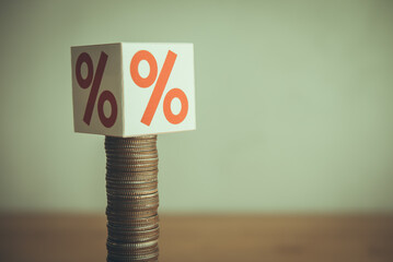 High interest rate (percentage sign) presses on slow growth stack coins on wooden table. Interest...