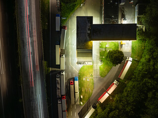A nocturnal aerial perspective of a gas station, with bay parking trucks positioned adjacent to the highway.