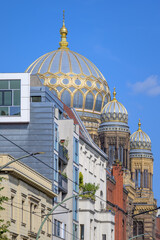 Golden domes of Neue Synagoge Berlin rise above nearby buildings against a blue sky.
