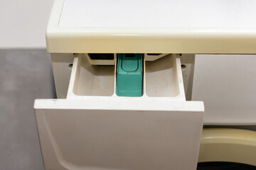 Top-down view of an open detergent drawer in an old washing machine, showing compartments for detergent and fabric softener.
