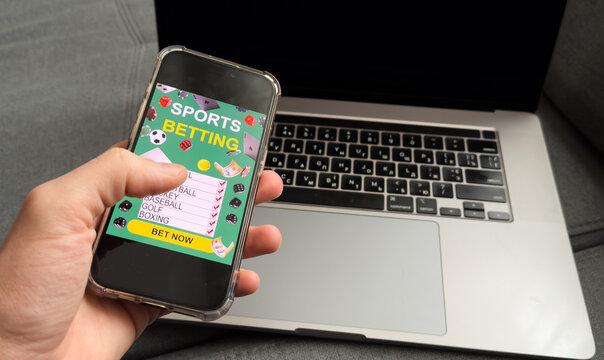 Close up of man holding smartphone with sports bets app to camera while watching football match at home, copy space