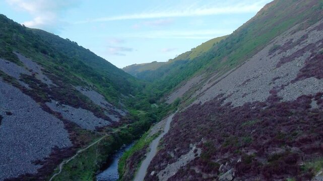 Rising Aerial View of Heddon Valley with Winding Paths and River at Sunrise with Sunlight Hitting Top of Valley. Rocks Lining Valley Side. Nature Drone Footage.