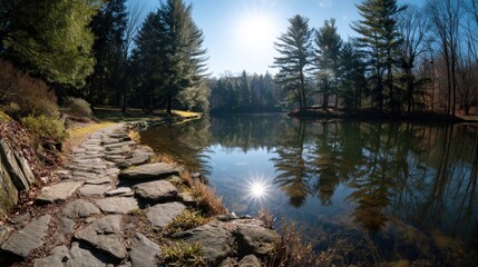 Scenic view of clear water lake reflecting trees under bright sun, with a stone trail leading through the park..