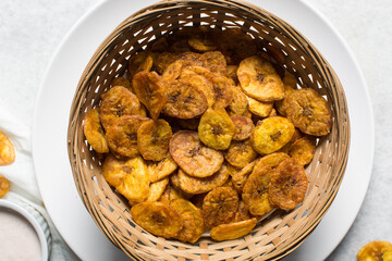 Overhead view of fried plantains chips in a basket, top view of fried ripe plantains on a white background