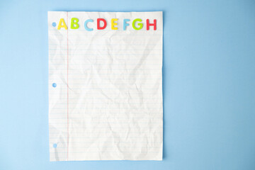 Crumpled, white, lined notebook paper with red, blue, green, and yellow letters at top on a blue...