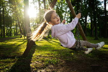 Young girl swinging in a green forest with evening sunlight