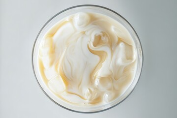 Top-down view of iced coffee with milk swirling in glass on a bright surface