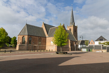 The Hervormde Kerk (Reformed Church) in Lexmond, Netherlands, stands to historical Dutch architecture. Its Gothic style, red brick, and tall spire dominate the village skyline under a serene sky.