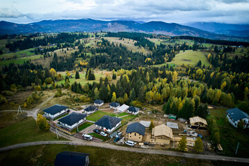 Aerial view of holiday cottages in mountains. Rest houses with photovoltaic solar panel system on roof in coniferous forest. Relaxing far from big city.