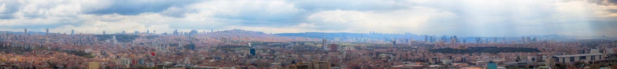 Wide panoramic view of Ankara city skyline with urban buildings, hills, and cloudy sky. Capital of Turkey showing modern and traditional elements blending in vibrant cityscape.

