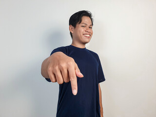 A smiling young Asian man wearing a blue shirt points down © Ichsan Gallery
