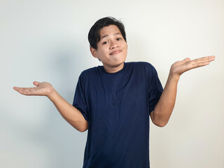 A young Asian man wearing a blue shirt shows confusion by shrugging his shoulders and opening his...