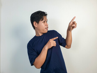 A young Asian man in a blue shirt looks surprised, pointing enthusiastically at something off-frame...