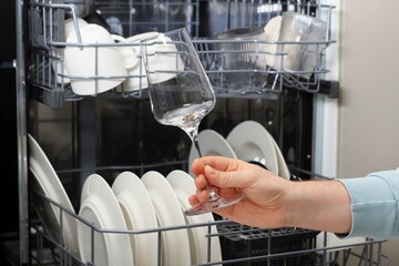 Man holding a wine glass near open dishwasher filled with clean dishes and glassware in a kitchen
