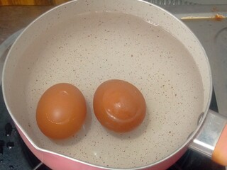 Two brown chicken eggs being boiled in a pot of water on a stove