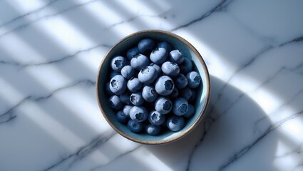 Bowl of fresh blueberries on a marble surface with soft sunlight and shadows