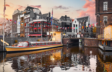 Amsterdam, Holland, Netherlands. Amstel river, canals and pleasure boat for city tours. Evening dusk sunset sky cityscape. Travel destination amsterdam for touristic tour entertainment travel.