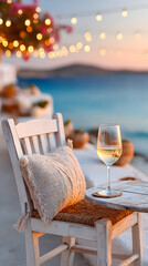 Elegant white chair with cozy cushion and glass of wine on table, surrounded by beautiful seaside ambiance and twinkling lights at sunset. Selective focus